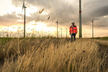 Engineer walking amidst grass at wind farm - UUF29289