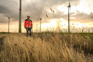 Engineer walking amidst grass at wind farm - UUF29291