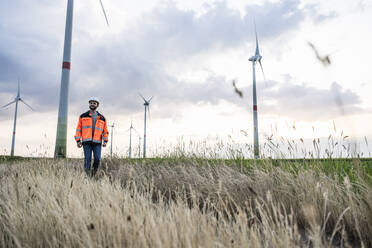 Engineer walking in grass at wind farm - UUF29294