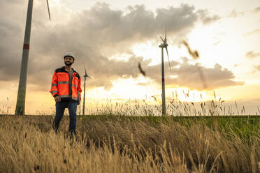 Engineer walking amidst grass on field in front of wind turbines - UUF29295