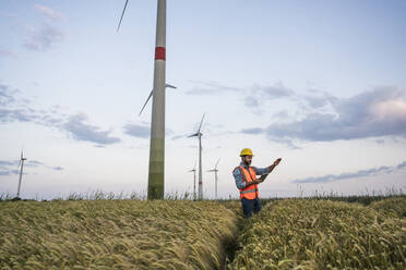 Engineer in reflective clothing using tablet PC standing in field at wind farm - UUF29304