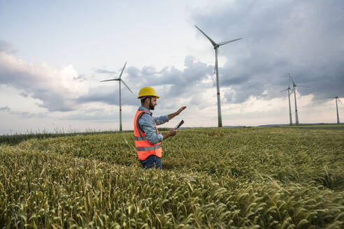 Ingenieur in reflektierender Kleidung bei der Arbeit mit einem Tablet-PC im Feld eines Windparks - UUF29306