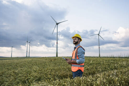 Ingenieur mit Tablet-PC auf einem Feld mit Windkraftanlagen im Hintergrund - UUF29307