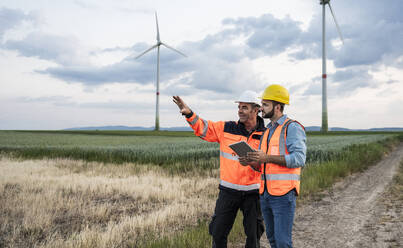 Engineer gesturing and explaining colleague at wind farm - UUF29312