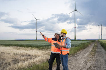 Engineer gesturing and explaining colleague at wind farm - UUF29313