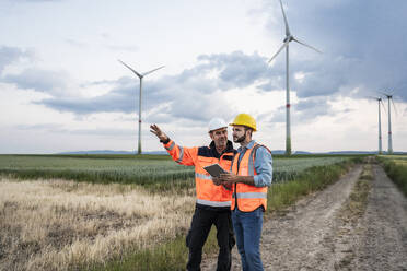 Engineer explaining colleague with tablet PC at wind farm - UUF29314