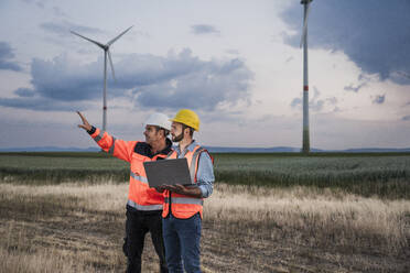 Engineers discussing together with laptop at wind farm - UUF29325