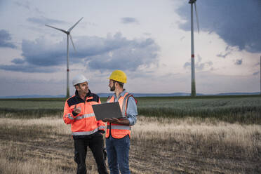 Ingenieure diskutieren im Windpark bei Sonnenuntergang - UUF29326