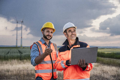 Lächelnde Ingenieure arbeiten mit Laptop im Windpark - UUF29328