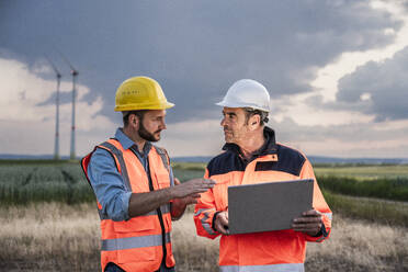 Engineer discussing with colleague at wind farm - UUF29329