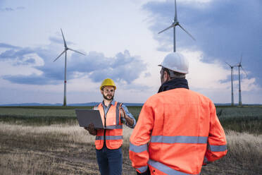 Ingenieur mit Laptop bei der Diskussion mit einem Kollegen im Windpark - UUF29332