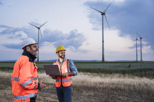 Lächelnde Ingenieure mit Laptop im Windpark - UUF29334