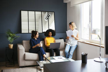 Multirassische Geschäftsfrauen, die im Büro auf dem Sofa sitzend diskutieren - EBSF03651