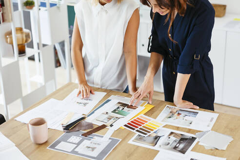 Colleagues discussing strategy over documents at desk in creative office - EBSF03656