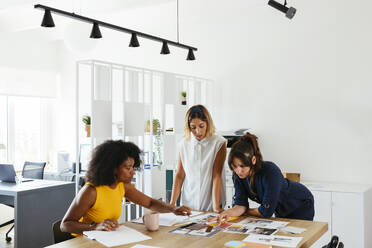 Multiracial business colleagues discussing over documents at creative office - EBSF03660