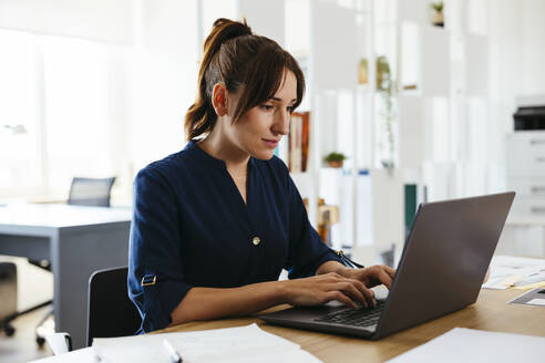 Businesswoman working on laptop at desk in creative office - EBSF03662