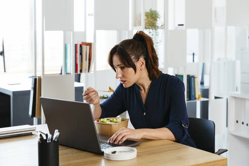Geschäftsfrau beim Mittagessen und bei der Arbeit am Laptop im Büro - EBSF03675
