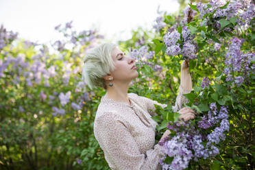 Portrait of woman smelling lilac flowers in garden - TETF01988