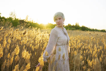 Portrait of woman standing in field at sunset - TETF02052