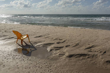 Plastic chair on sunny wet, sandy ocean beach, Bat Yam, Israel - FSIF06319