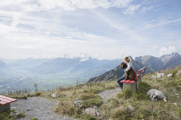Girl with dogs sitting on bench enjoying scenic, majestic sunny mountain range view, Switzerland - FSIF06326