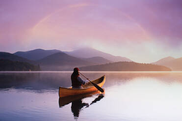 USA, St. Armand, Rear view of woman canoeing on calm Lake Placid at sunset in Adirondack Park - TETF02059
