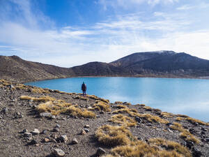 New Zealand, Waikato, Tongariro National Park, Hiker standing by lake in Volcanic landscape - TETF02079