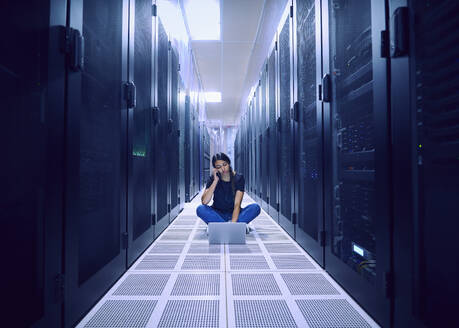 Female technician using laptop and phone in server room - TETF02139