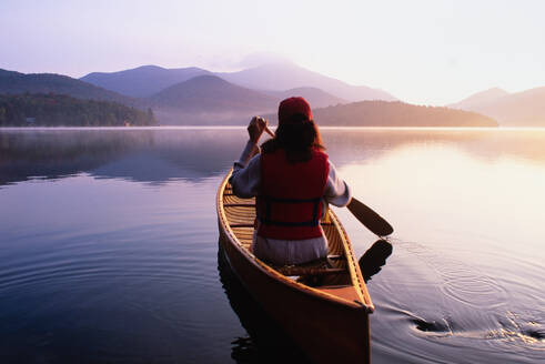 United States, New York, Rear view of woman paddling canoe on Lake Placid at sunrise, Adirondacks State Park - TETF02161
