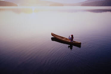 High angle view of woman paddling canoe on Lake Placid at sunrise, Adirondacks State Park - TETF02163