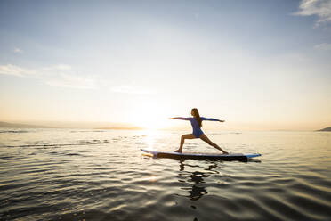 Woman doing yoga on paddleboard at sunset - TETF02165