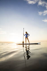 Woman standing on paddleboard at sunset - TETF02166