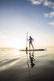 Woman standing on paddleboard at sunset - TETF02166