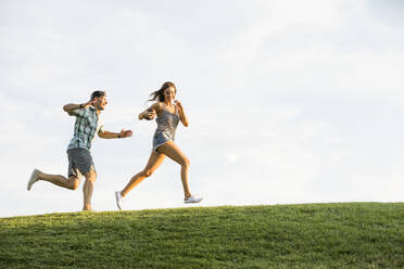 Woman and man running on grassy hill in park - TETF02168