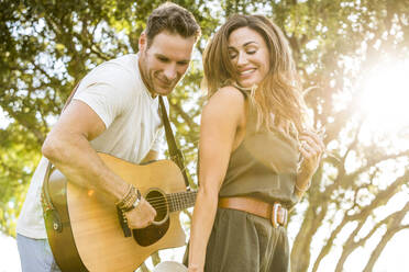 Woman dancing to music while man playing guitar in park - TETF02172