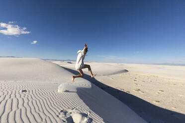 United States, New Mexico, White Sands National Park, Teenage girl leaping on sand dunes - TETF02188