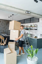 Full body side view of male in casual clothes carrying carton boxes with belongings while moving into new apartment - ADSF44414