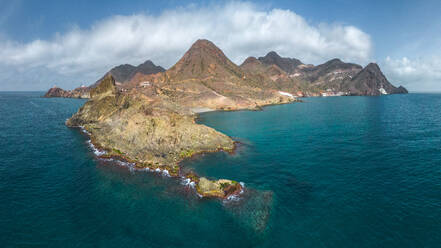 Drone view of rough rocky formations located near rippling sea against cloudy blue sky in Almeria - ADSF44423