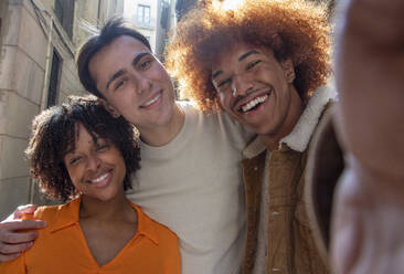 Eine bunt gemischte Gruppe von Freunden posiert für ein Selfie auf der Straße, wobei ein glücklicher schwarzer Mann seinen Arm ausstreckt - ADSF44426