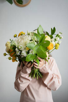 Unrecognizable girl holding bouquet of fresh roses of yellow white colored flowers buds with green leaves stem against gray background - ADSF44429