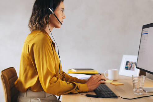 Telecommunications agent working in a call center. She wears a headset and sits in front of a computer in the office, handling incoming calls and providing virtual assistance to customers and clients. - JLPPF02078