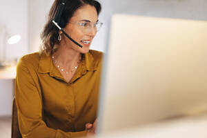Female call center operator delivering travel consultation services for an online travel agency. With a headset on, she engages in a conversation with a client and assists in travel booking and planning. - JLPPF02082