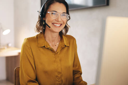 Caucasian call center agent working in a professional setting. She is wearing a headset and sitting at her workstation, ready to answer calls and assist customers with their inquiries. - JLPPF02084