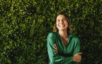 Businesswoman celebrates her success in implementing eco-friendly practices. Female professional showing her joy and pride in her company's environmental responsibility as she stands in a green office. - JLPPF02111