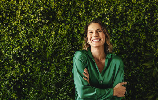 Businesswoman celebrates her success in implementing eco-friendly practices. Female professional showing her joy and pride in her company's environmental responsibility as she stands in a green office. - JLPPF02111