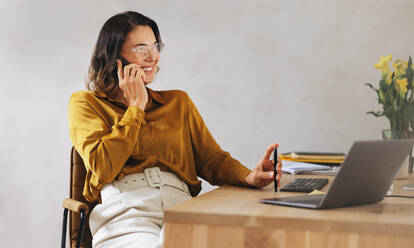 Caucasian businesswoman engages in a phone call discussion in her office. Professional web designer demonstrating effective communication skills as she handles her business responsibilities over the phone. - JLPPF02112