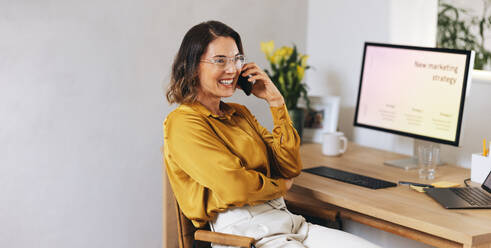 Caucasian businesswoman engages in a phone call while seated at her desk. Woman working with a creative and digital marketing mindset, focused on planning a marketing campaign and developing a strategic approach for success. - JLPPF02117