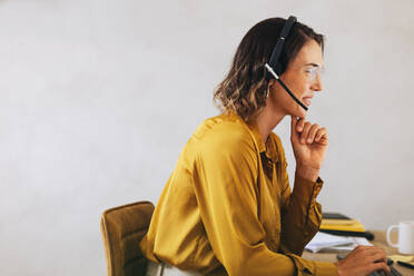 Contact center employee talking to calling customers through her headset, efficiently handling their enquiries. Woman delivering excellent customer service in a telecommunications role. - JLPPF02123