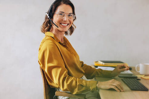 Customer service consultant smiling at the camera while wearing a headset, demonstrating her expertise in customer support. Woman excelling in her role as a professional call center agent. - JLPPF02129