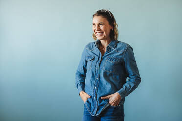 Professional business woman celebrating her success in a studio. Caucasian woman smiling happily in denim clothing, portraying the modern entrepreneurial spirit. - JLPPF02136